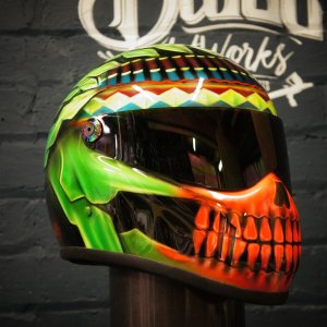 Custom painted motorcycle helmet featuring vibrant green and orange skull design with detailed teeth and jaw, tribal geometric patterns on top