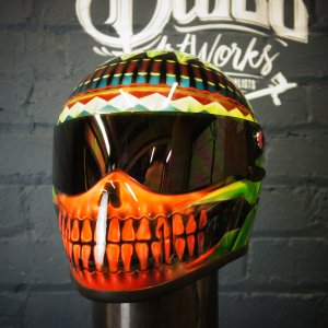 Vibrant skull motorcycle helmet with orange teeth design, tribal patterns on top, geometric colorful bands around crown