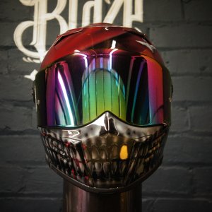 Red motorcycle helmet featuring chrome skull jaw design with iridescent rainbow visor and metallic silver airbrush finish
