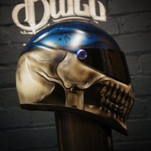 Photorealistic skull motorcycle helmet with metallic gold skull face, blue bandana with paisley pattern, glowing blue eye