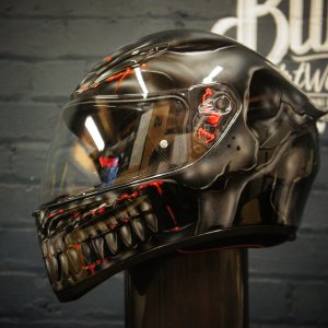 Black motorcycle helmet with metallic chrome skull design featuring glowing red cybernetic eye details and robotic jaw teeth