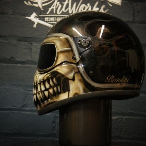 Black motorcycle helmet with realistic skull design airbrushed on side, featuring detailed bone structure and teeth in brown tones